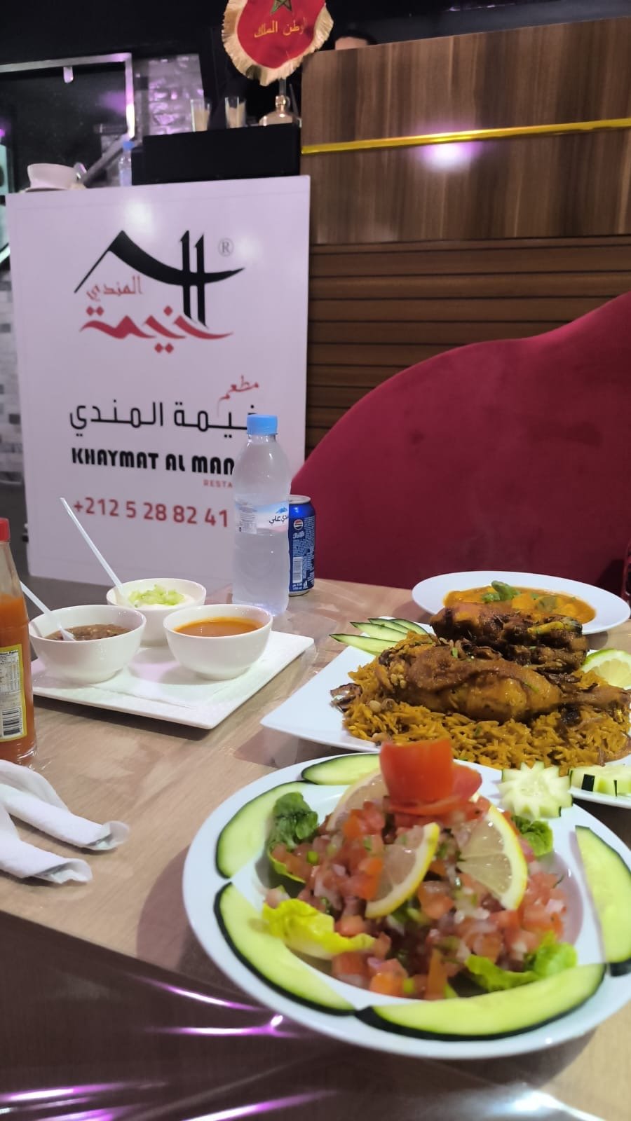 Table spread at Khaymat Al Mandi with mezze, chicken tagine and fresh salad, restaurant branding in the background